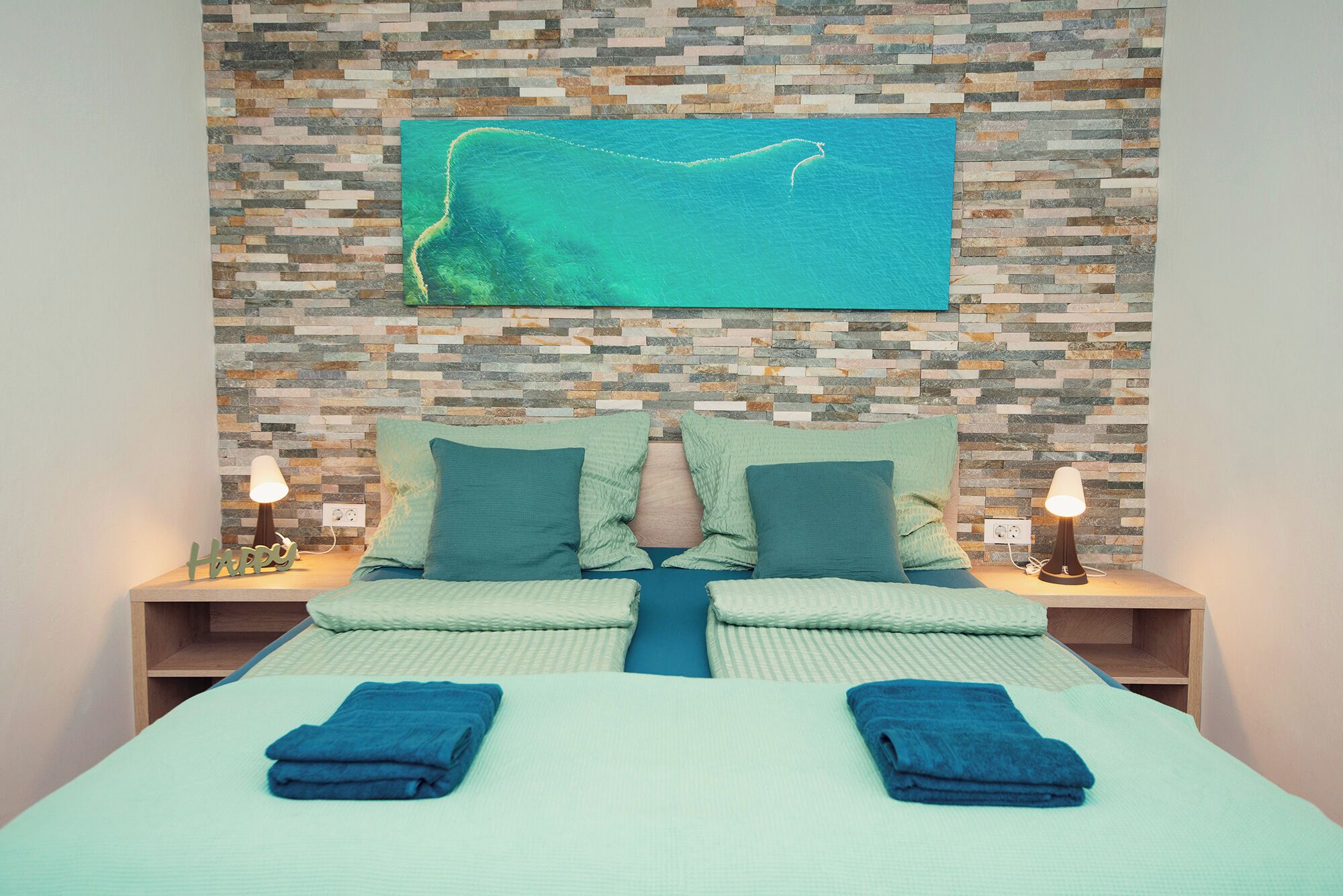 Une chambre d’hôtel avec un lit, deux tables de chevet, un téléviseur fixé au mur et un mur décoré de mosaïques.
