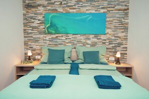 Habitación de hotel con cama, dos mesitas de noche, televisor montado en la pared y un muro de mosaicos.