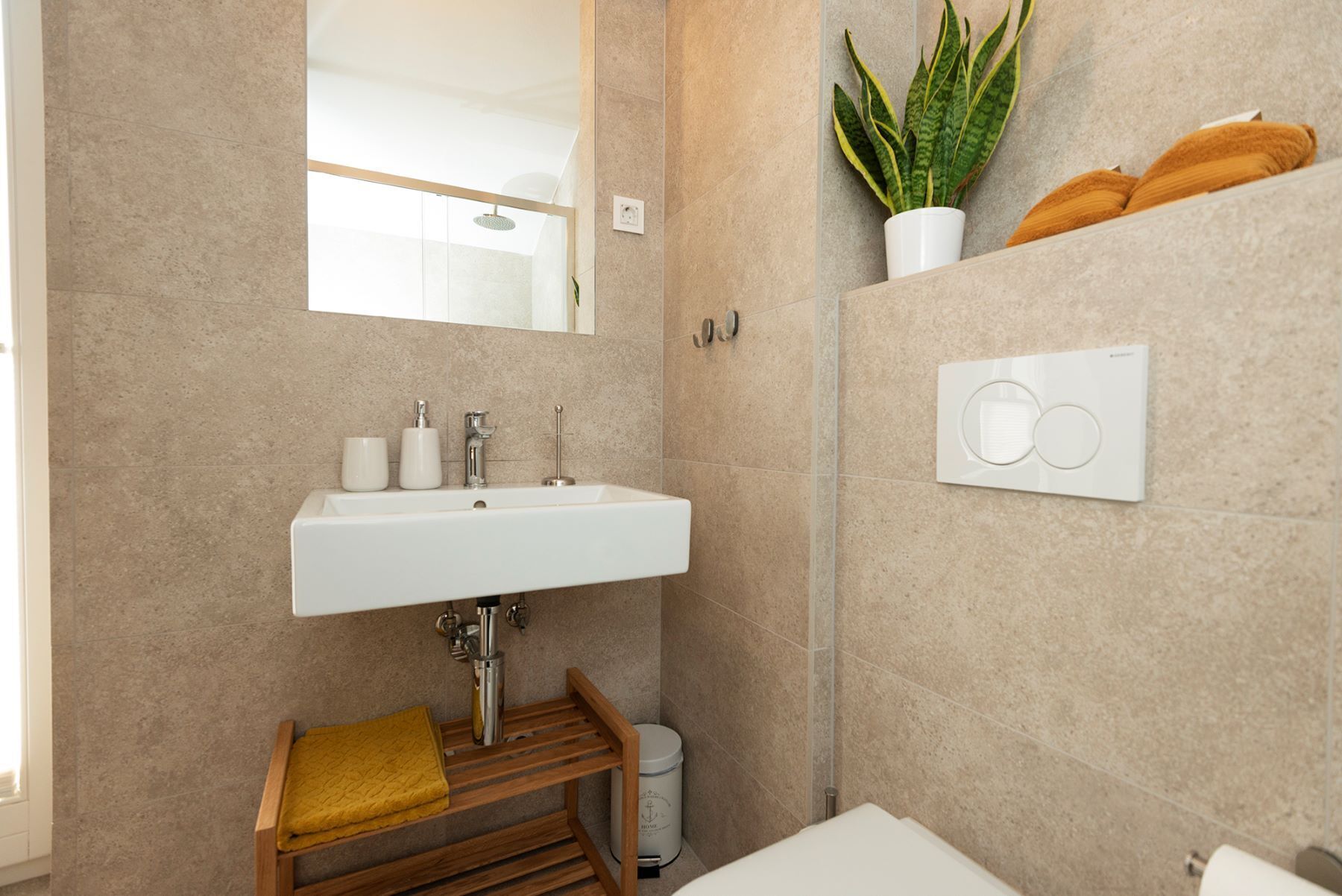 A modern bathroom with a white sink, mirror, and a potted plant.