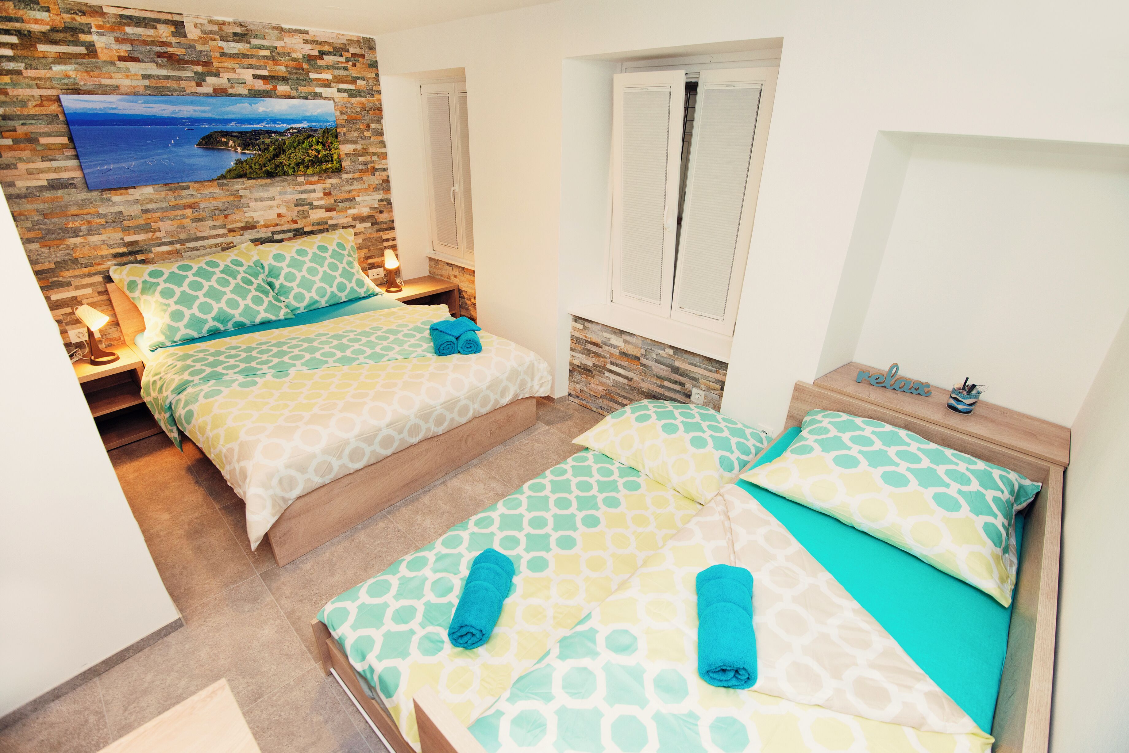 Un dormitorio con dos camas, una pared de piedra, una ventana y un cuadro.