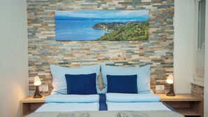 A bedroom with a bed, two bedside tables, two lamps, a painting of a coastal landscape, and a window with blinds. - Old Town Rooms Piran (Piran)