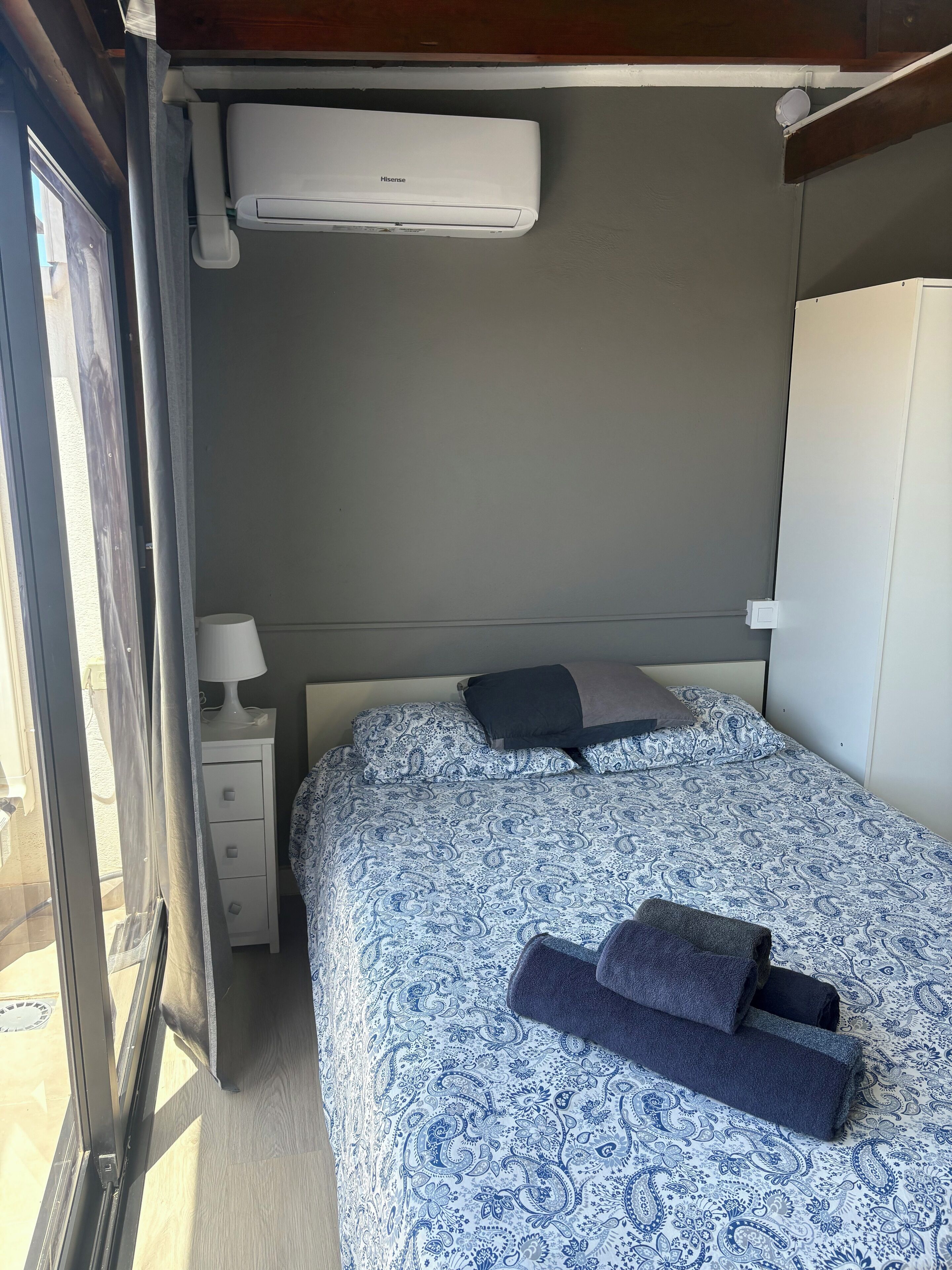 Ein Schlafzimmer mit einem Bett, einem Nachttisch, einer Lampe und einer Klimaanlage.