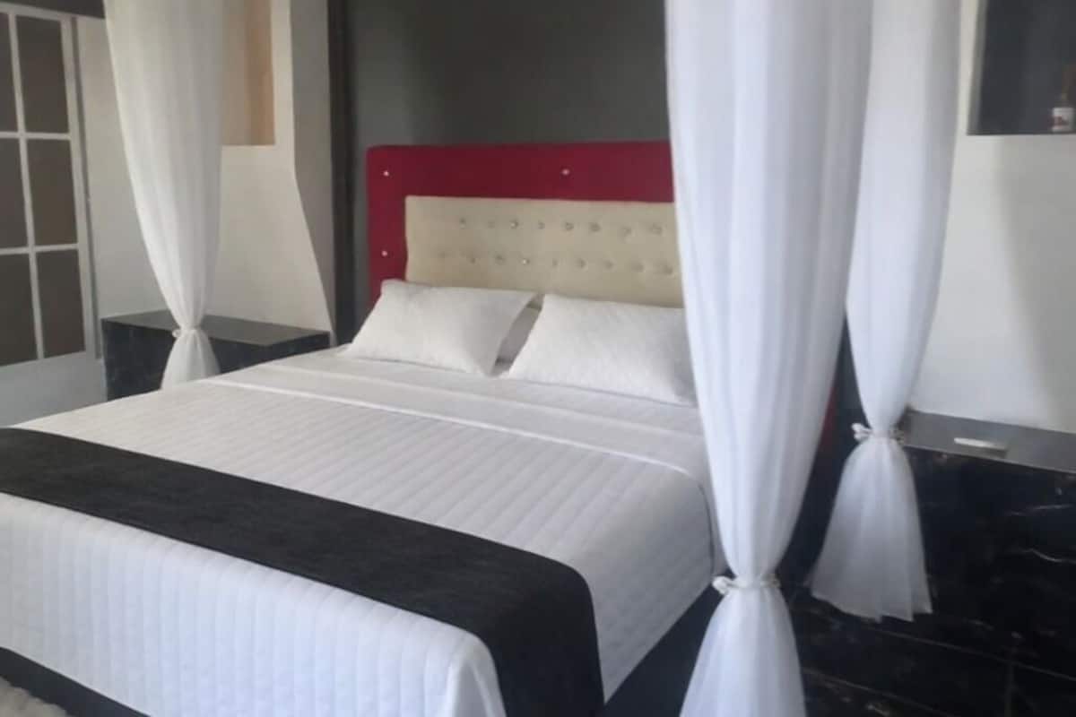 A bed with white bedding, a red headboard, and white curtains.