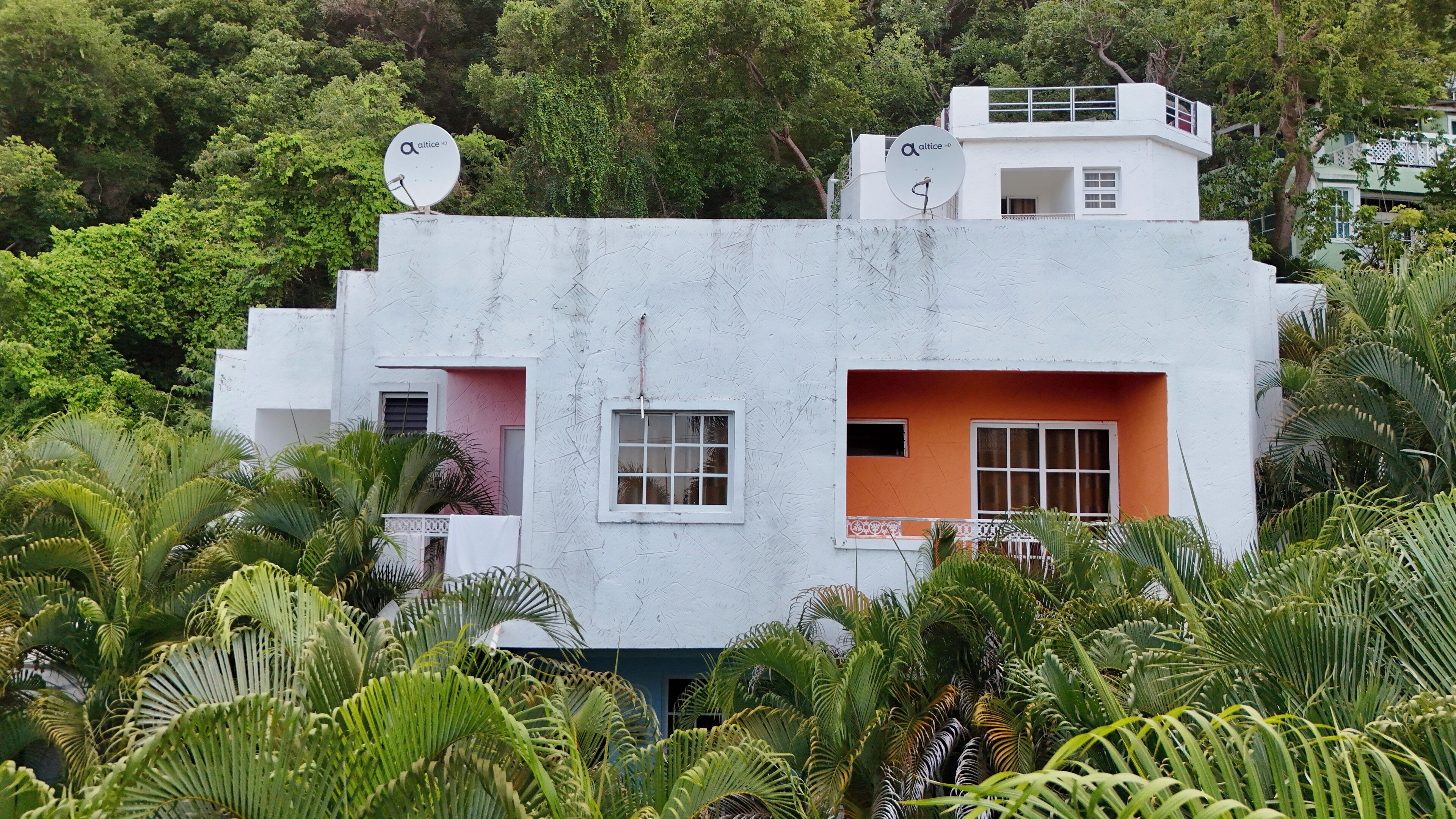 Un edificio blanco con antenas satelitales, rodeado de abundante vegetación.