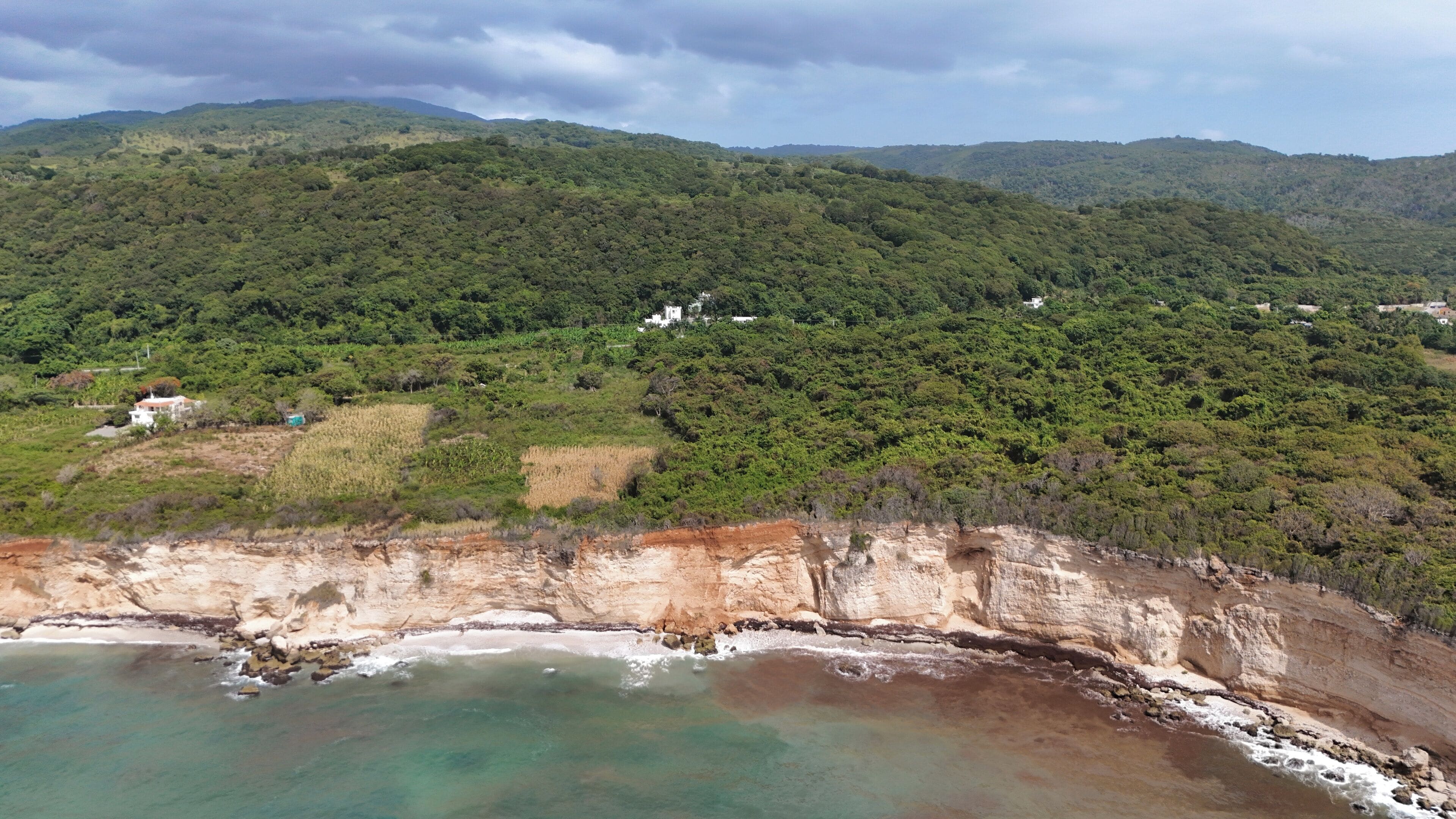 Paisaje costero con un acantilado, playa y colinas boscosas.