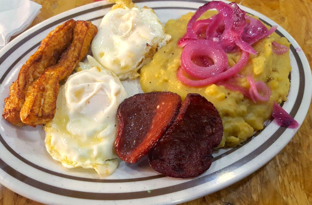 A plate with scrambled eggs, fried plantains, and a slice of red meat.