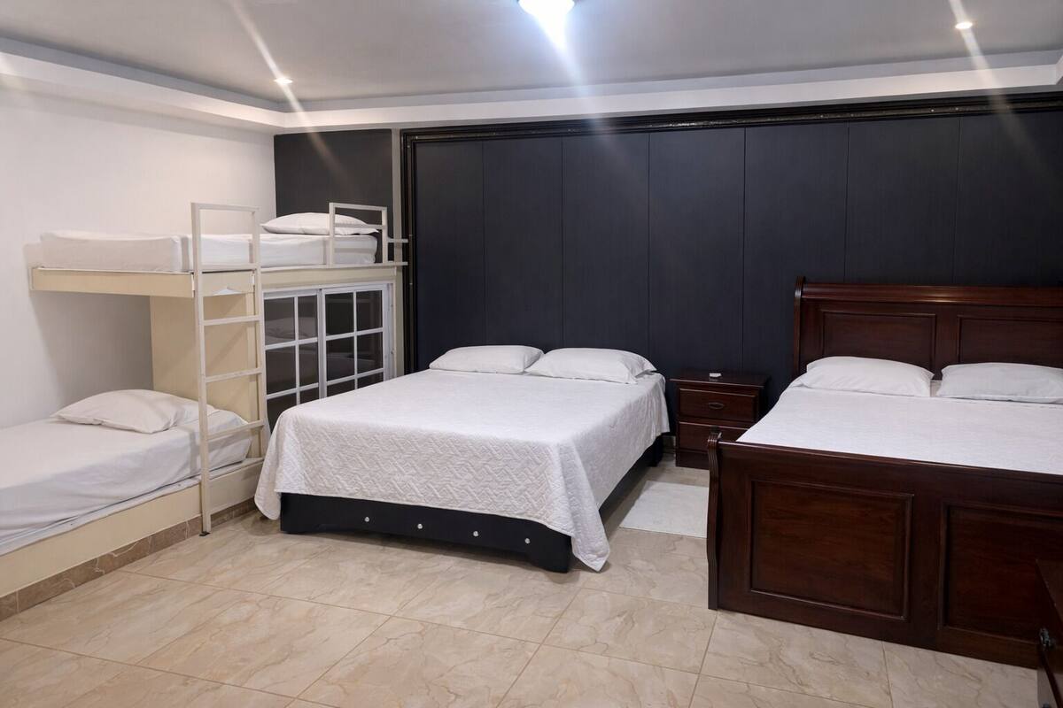 A bedroom with bunk beds, a single bed, a wooden headboard, a nightstand, and a dark wall.