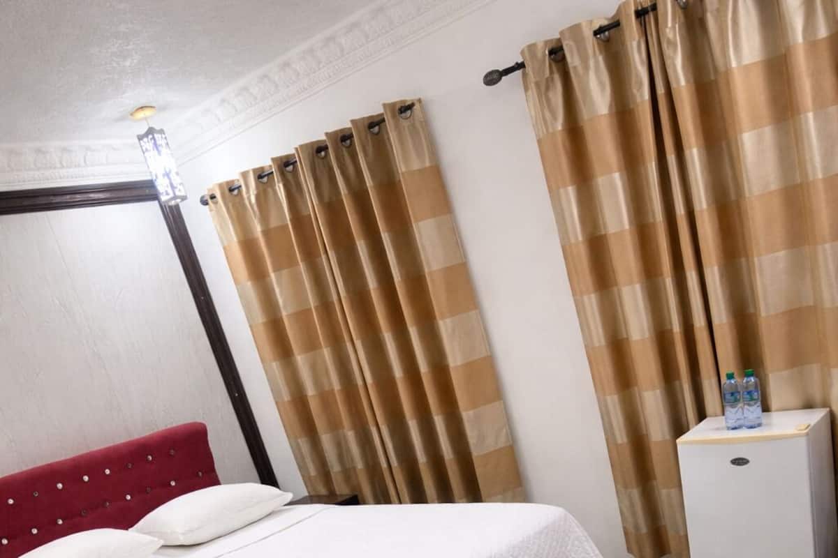 A hotel room with a bed, a small white refrigerator, and beige curtains.