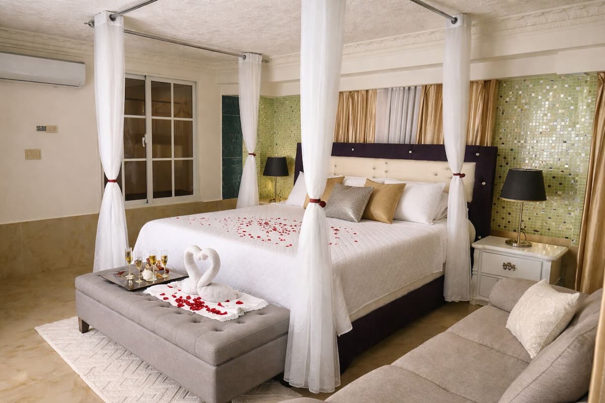 A four-poster canopy bed with a white bedspread, a bedside table with a lamp, and a seating area with a sofa.