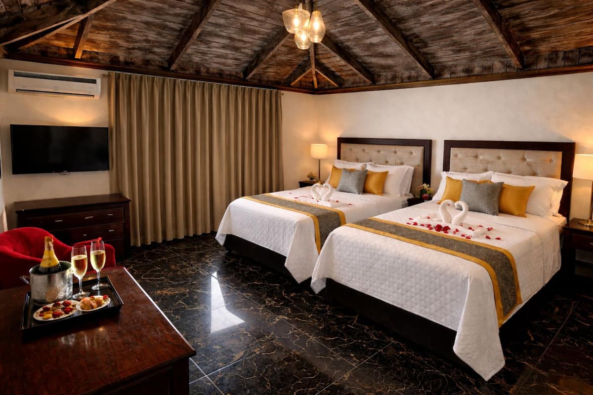 A hotel room with two beds, a TV, a minibar, and a dining table with a bottle and glasses.