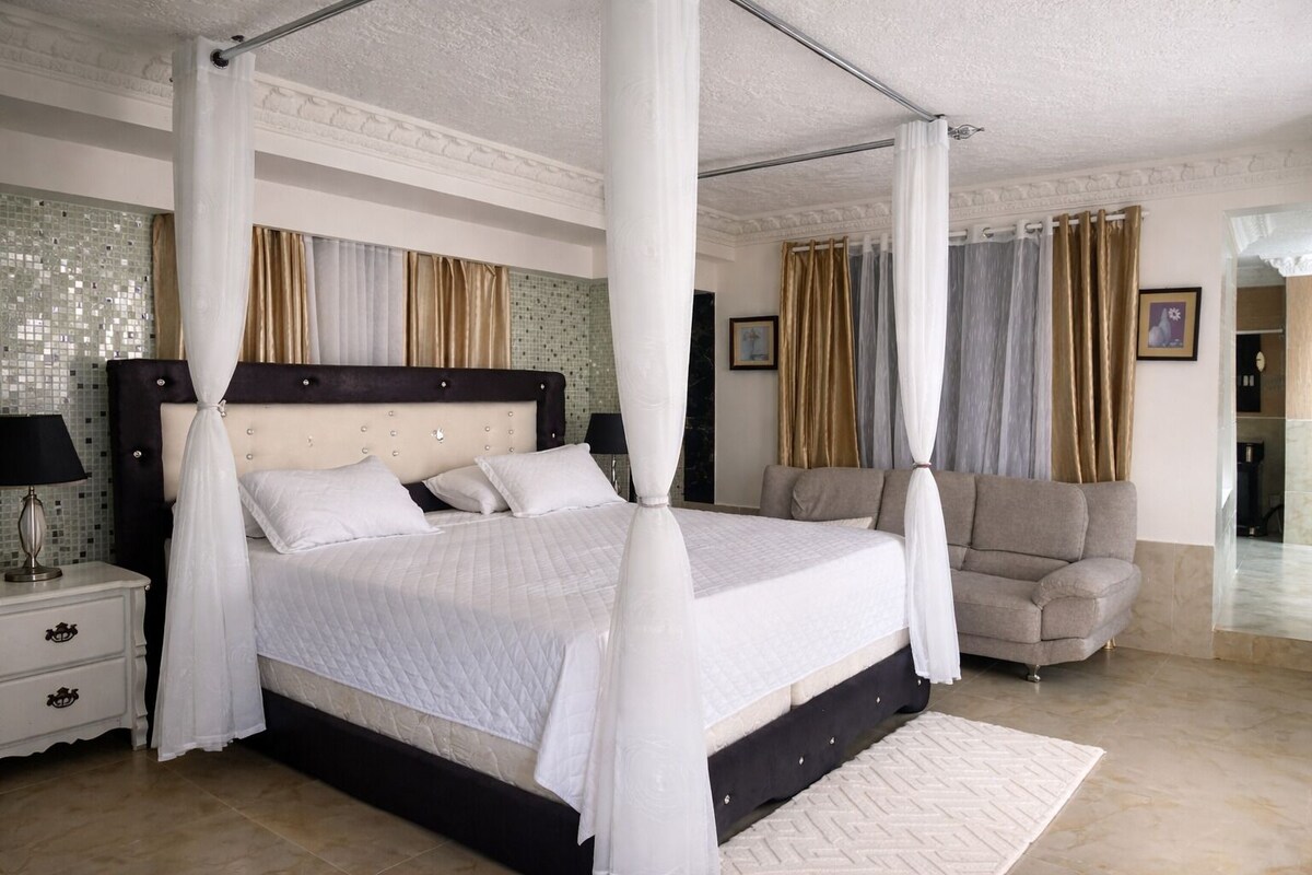A bedroom with a four-poster bed, a nightstand, a sofa, and a mirror.