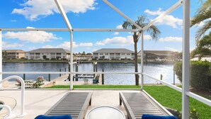 A covered outdoor area with a view of a canal, lounge chairs, and a table. - Entire Waterfront Duplex - Pool & Spa - 4BR/4BA (Cape Coral)