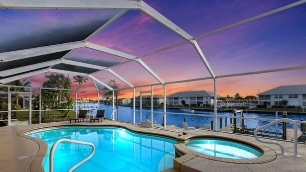 An indoor swimming pool with a covered area, a view of the water, and a sunset in the background. - Entire Waterfront Duplex - Pool & Spa - 4BR/4BA (Cape Coral)