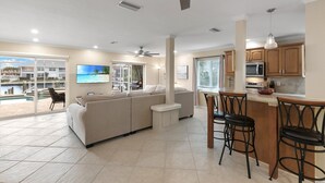 A modern living room with a large sectional sofa, a dining area with bar stools, and a kitchen with wooden cabinets and a bar. - Entire Waterfront Duplex - Pool & Spa - 4BR/4BA (Cape Coral)