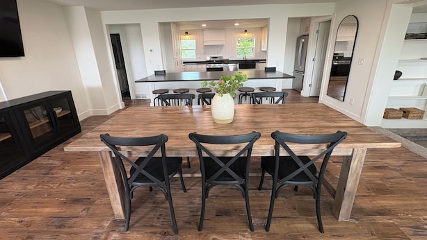 A spacious kitchen with a central island, wooden dining table with chairs, and a large window providing natural light.