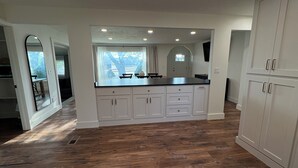 A spacious kitchen with white cabinetry, a wooden floor, and a large window providing natural light.