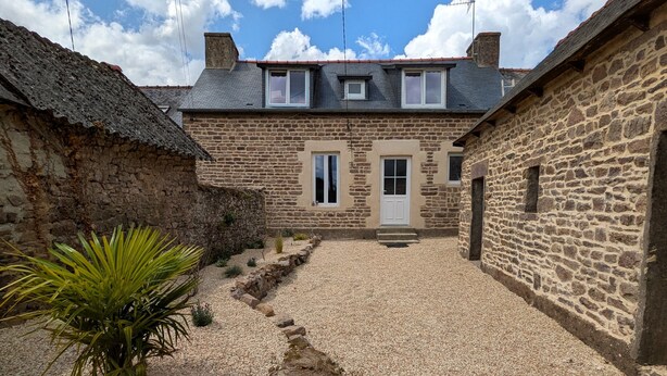 A courtyard with stone walls, a gravel path, and a door leading to a building with a sloped roof.