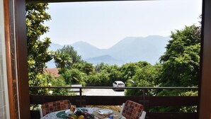 A balcony with a table set for breakfast, overlooking a road and mountains.