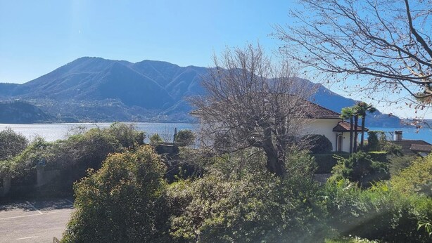 A coastal view with a mountain in the background, a building with a red roof, and dense greenery in the foreground.