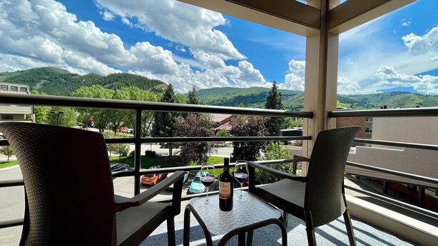 A balcony with a table and chairs, overlooking a street and green hills.
