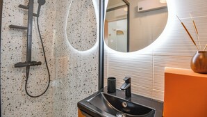 Un baño moderno con ducha independiente, un lavamanos con grifo negro y un espejo redondo.