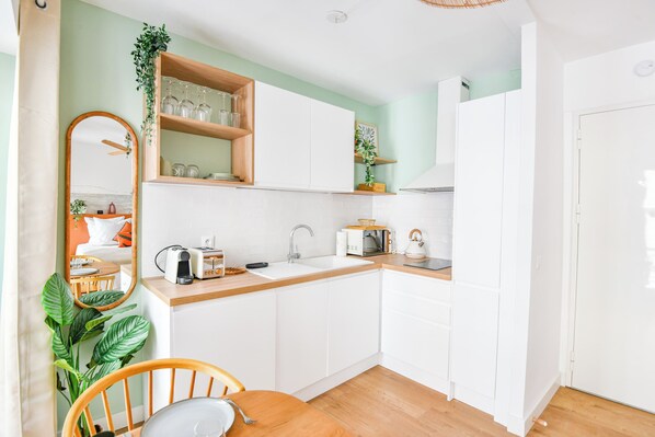 Una cocina compacta con armarios blancos, encimera de madera, pileta, microondas y tostadora.