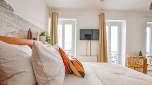 Un dormitorio con cama, almohadas, un televisor y un balcón con cortinas.