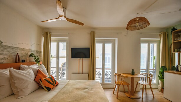 Un dormitorio con cama, televisión, balcón y zona de comedor.