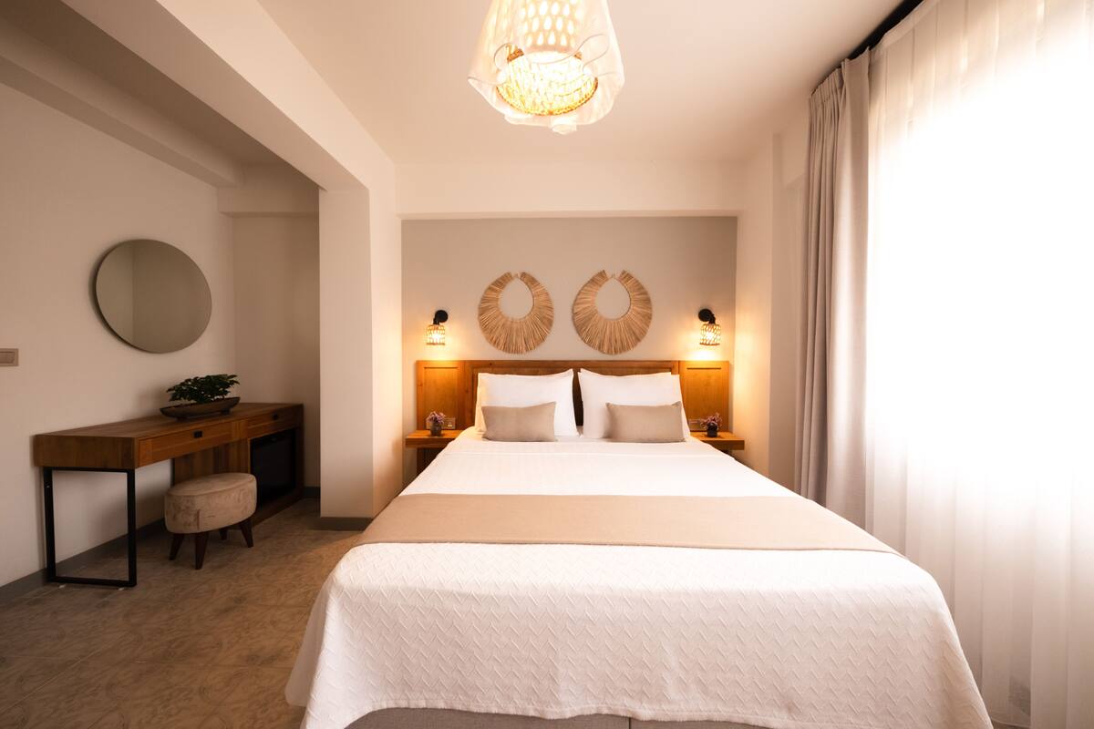 Un dormitorio ordenado con una cama grande, mesitas de noche con lámparas, un espejo redondo y un escritorio de madera.