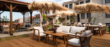 A wooden deck with outdoor furniture, including sofas and tables, and thatched umbrellas providing shade.