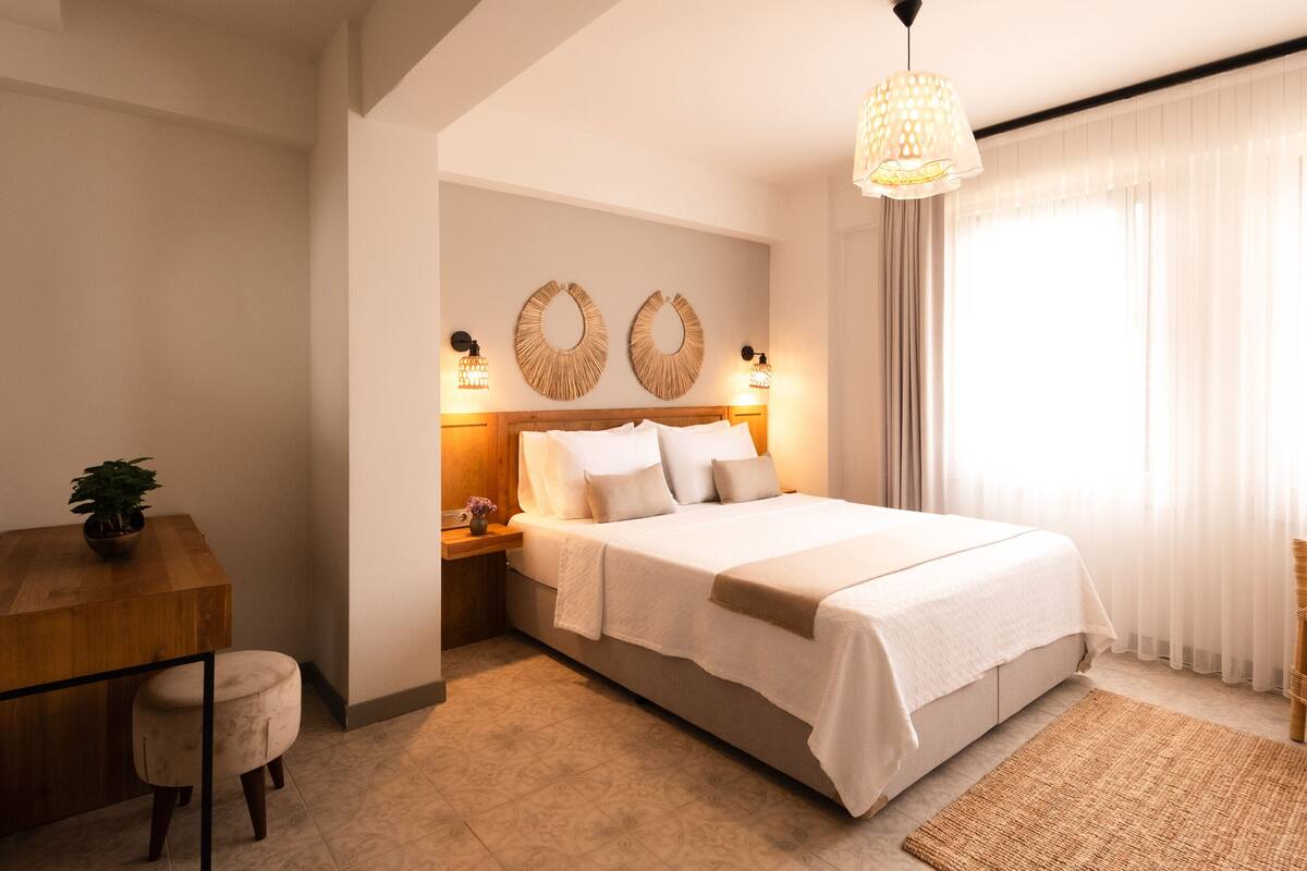 Un dormitorio con cama, mesitas de noche, un escritorio y una lámpara colgante.