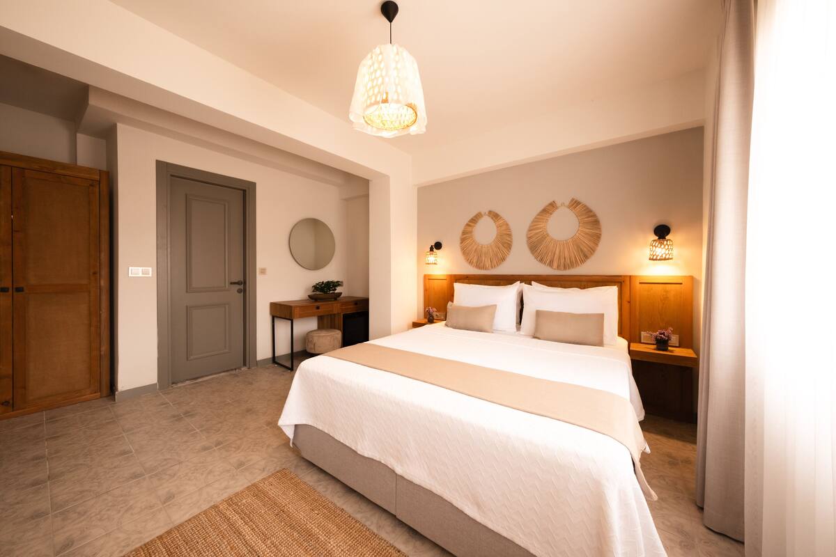 Un dormitorio con una cama grande, lámparas de noche, un armario de madera, un espejo redondo y una mesita con una planta.