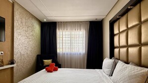 Habitación de hotel con una cama grande, una silla, un televisor y un ventanal con cortinas.