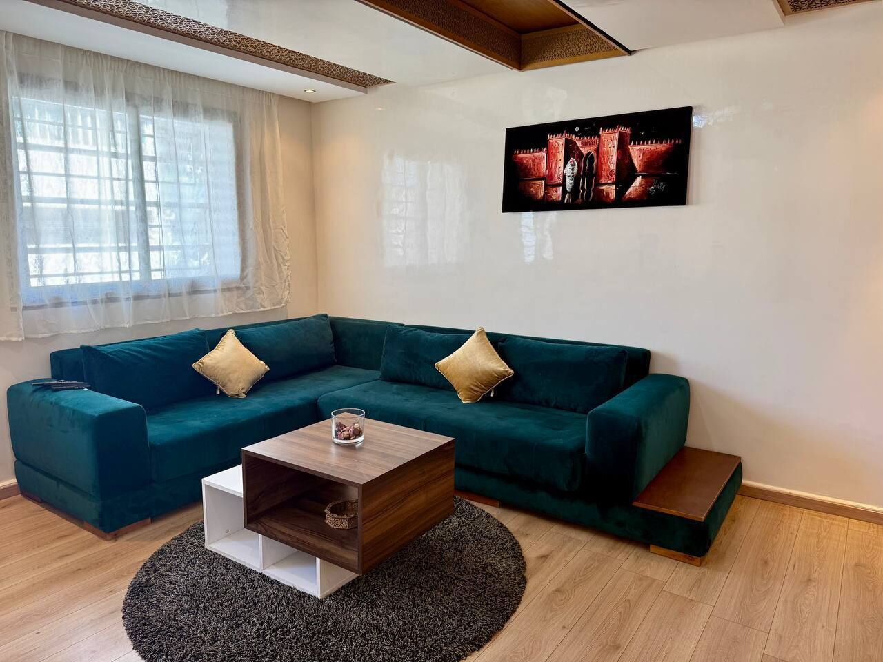 Ein modernes Wohnzimmer mit einem salbeengrünen Modulsofa, einem Holztisch und einem großen Gemälde an der Wand.