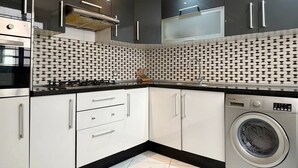 Una cocina moderna con armarios oscuros, una estufa de acero inoxidable, horno empotrado, lavadora y un salpicadero con diseño.
