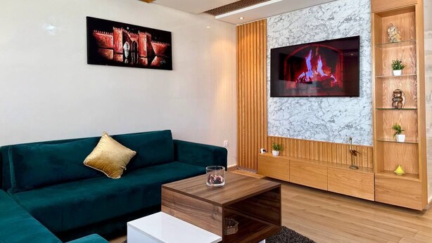 Una sala de estar moderna con un sofá verde, un televisor de pantalla plana montado en una pared de mármol y un mueble de entretenimiento de madera.