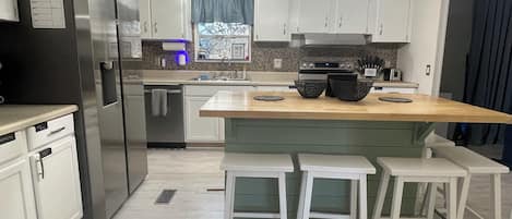 A modern kitchen with white cabinets, a stainless steel refrigerator, a wooden island with stools, and a built-in oven.