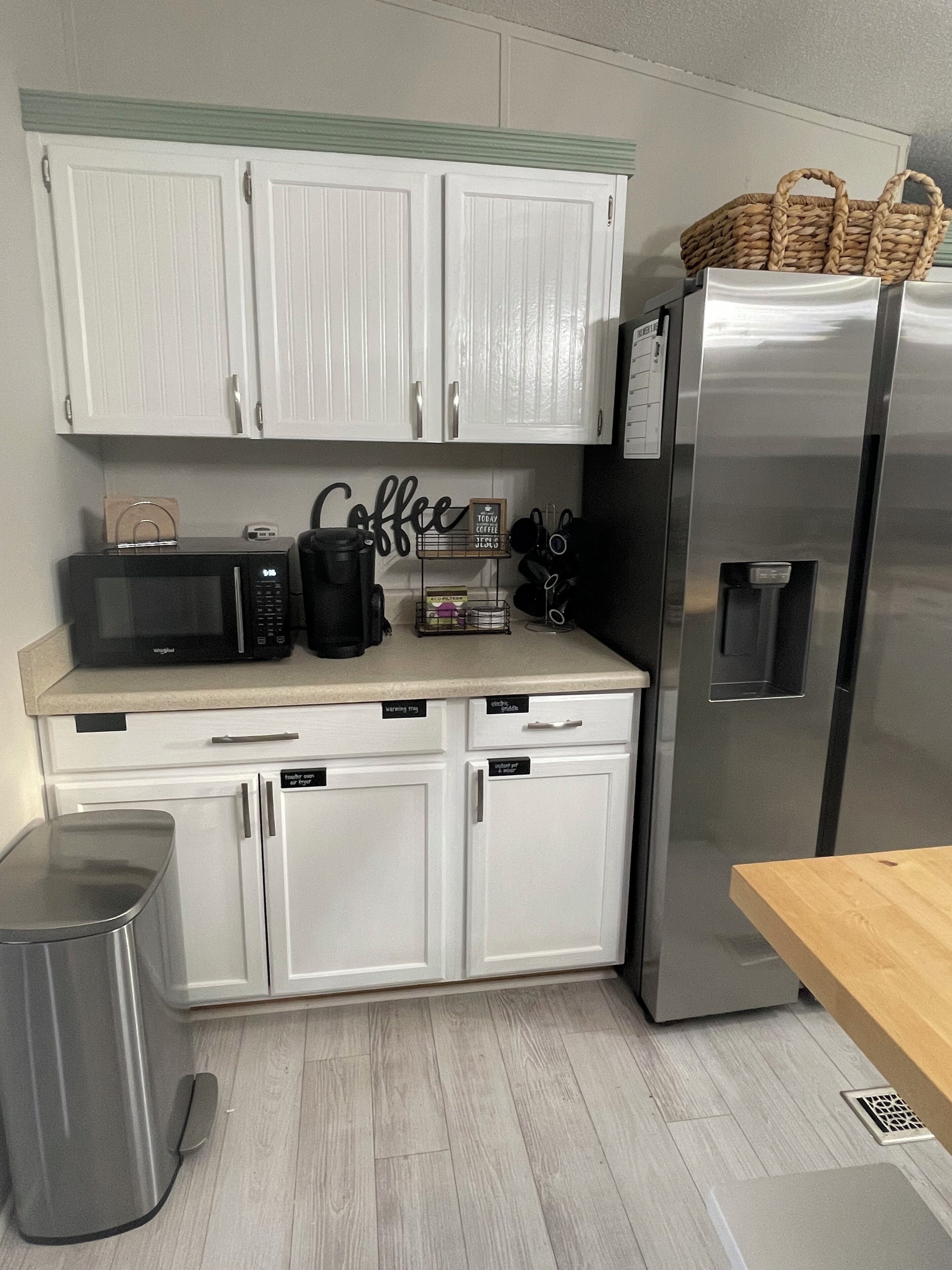 A compact kitchen with white cabinets, a stainless steel refrigerator, a microwave, and a coffee station.