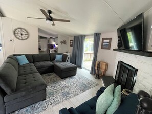 Uma sala de estar com sofá seccional, televisão de tela plana, lareira e ventilador de teto.