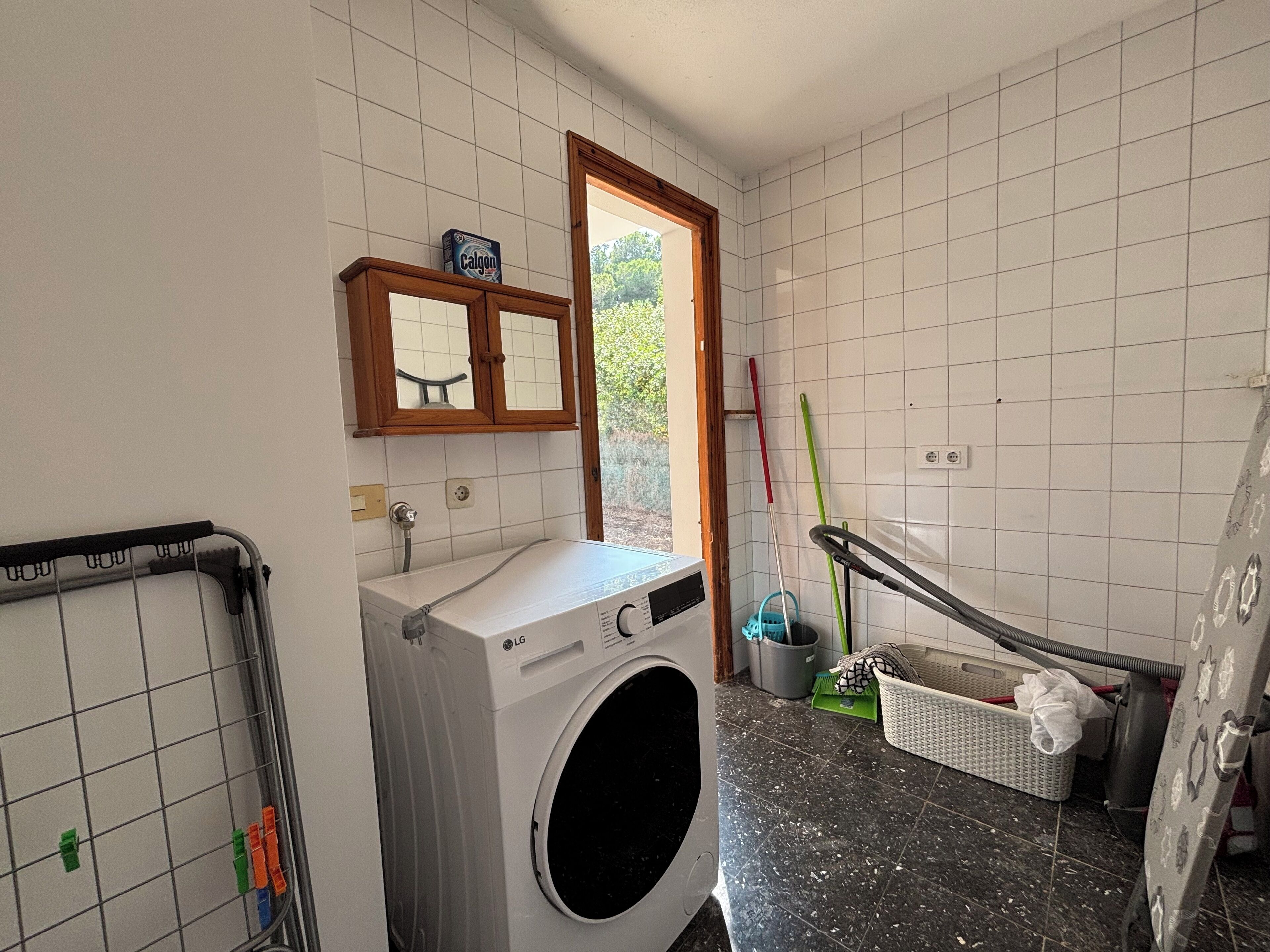 Une buanderie équipée d’un lave-linge, d’un étendoir et d’une fenêtre donnant sur un espace verdoyant.
