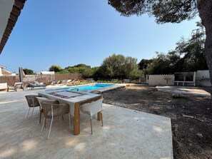 A poolside area with a table and chairs, a barbecue grill, and a stone wall. - Air-conditioned villa with private pool and large garden (Port d'Addaia)