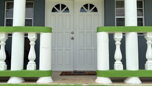 A two-story house with a green exterior, white columns, and a white front door with two windows.