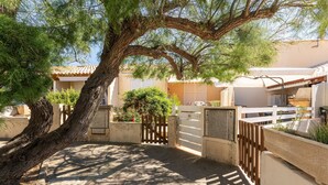 Una entrada con un muro de madera, un árbol grande y un edificio con tejado de baldosas.