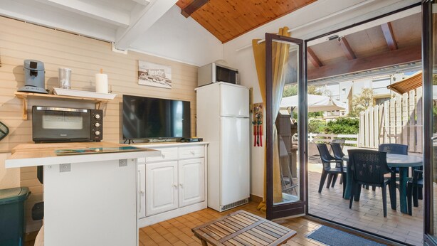Cocina compacta con microondas, horno y refrigerador, una pequeña mesa de comedor y una puerta corrediza de vidrio que da a un patio exterior.