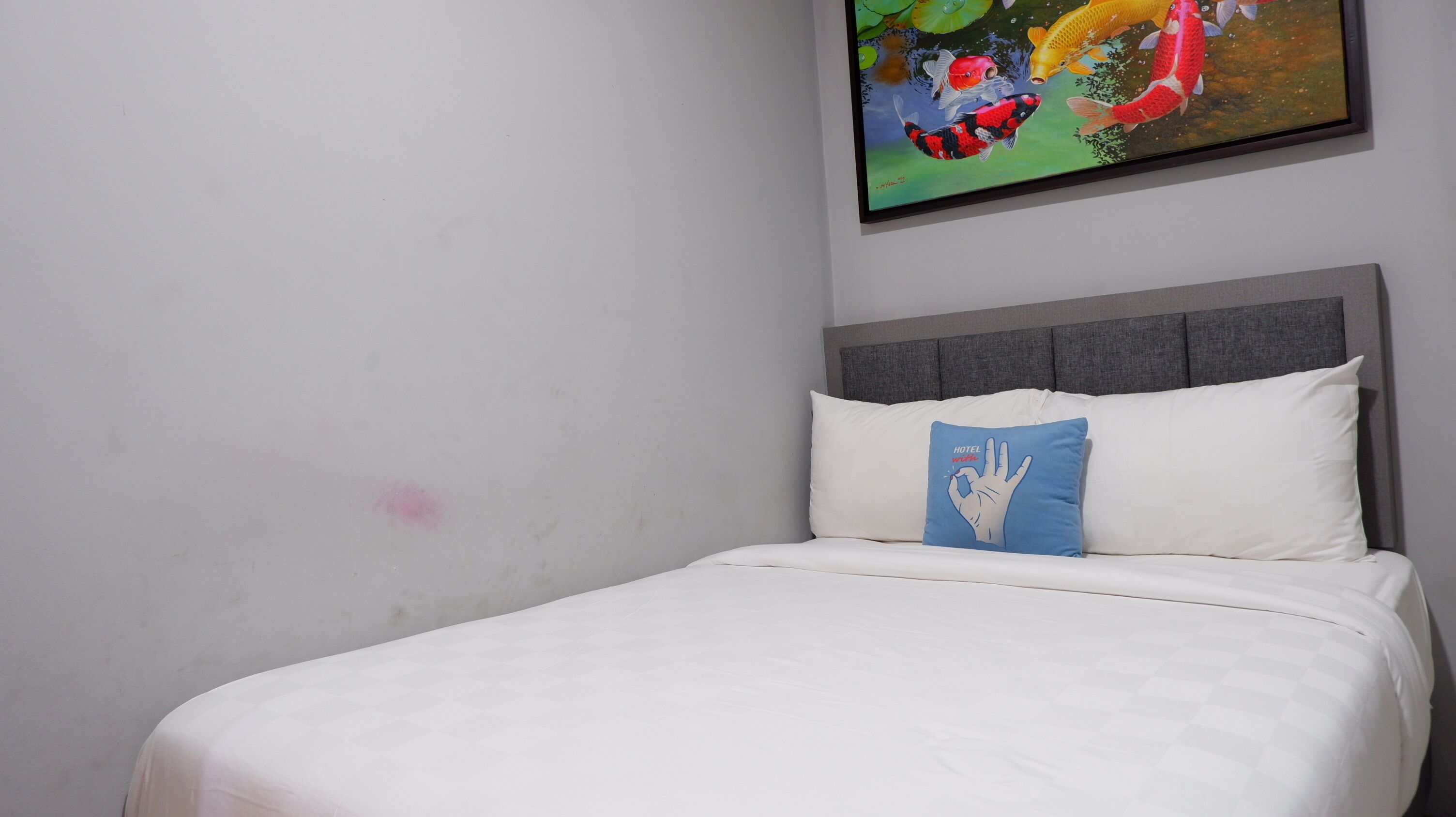 Habitació d'hotel amb un llit, un coixí amb un disseny d'empremta de mà i un quadre de peixos colorits a la paret.