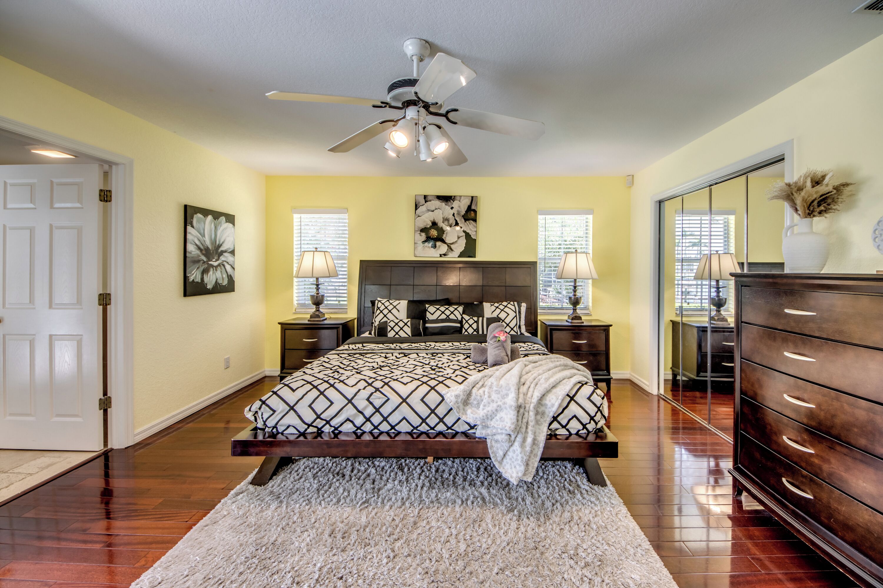 A bedroom with a bed, nightstands, a dresser, a ceiling fan, and a large mirror.