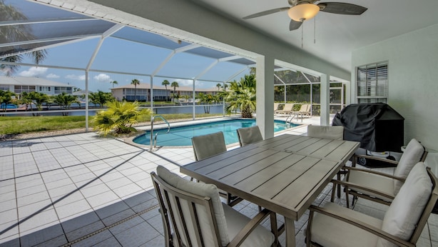 A covered outdoor area with a pool, a table and chairs, and a ceiling fan. - Heated Pool - Gulf Access WIDE canal with dock - BBQ - Large Backyard (Cape Coral)