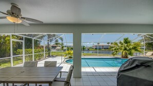 An outdoor patio with a pool, covered seating, and a ceiling fan. - Heated Pool - Gulf Access WIDE canal with dock - BBQ - Large Backyard (Cape Coral)