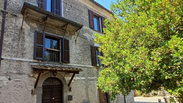 A stone building with a cobblestone street, a large tree, and a black door. - Bottino Palace - Vulsinia House (BOLSENA)