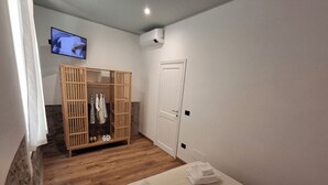 A bedroom with a bed, a wooden wardrobe, a television, and an air conditioning unit. - Bottino Palace - Vulsinia House (BOLSENA)